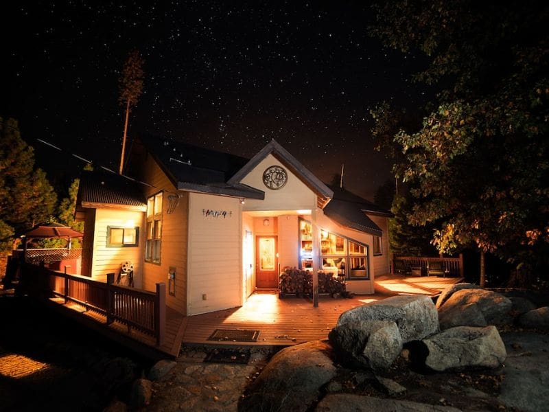 Nighttime view of The Ahweanee cabin near Yosemite illuminated under a starry sky, surrounded by trees.