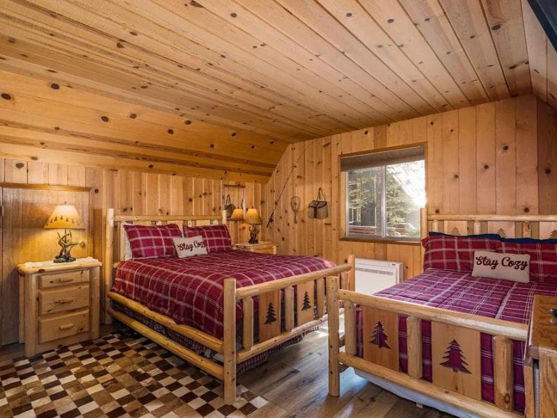 A warm, rustic bedroom featuring wood-paneled walls, two beds with red plaid bedding in a Yosemite cabin rental.