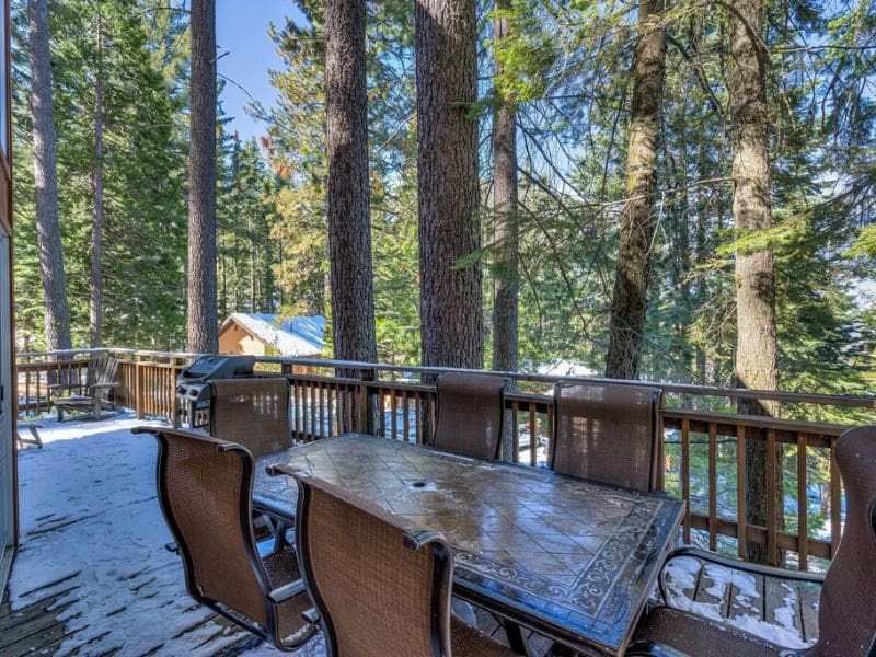 Deck Area at Yosemite Vista Cabin. An outdoor dining area on the deck surrounded by towering trees, complete with a grill and a large table.