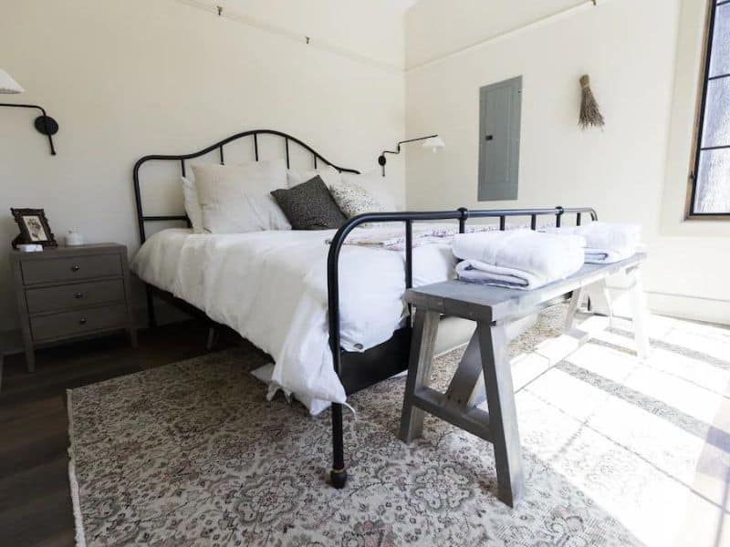 Bedroom in a Hocking Hills vrbo cottage with a wrought-iron bed, area rug, and wooden bench with towels on it.