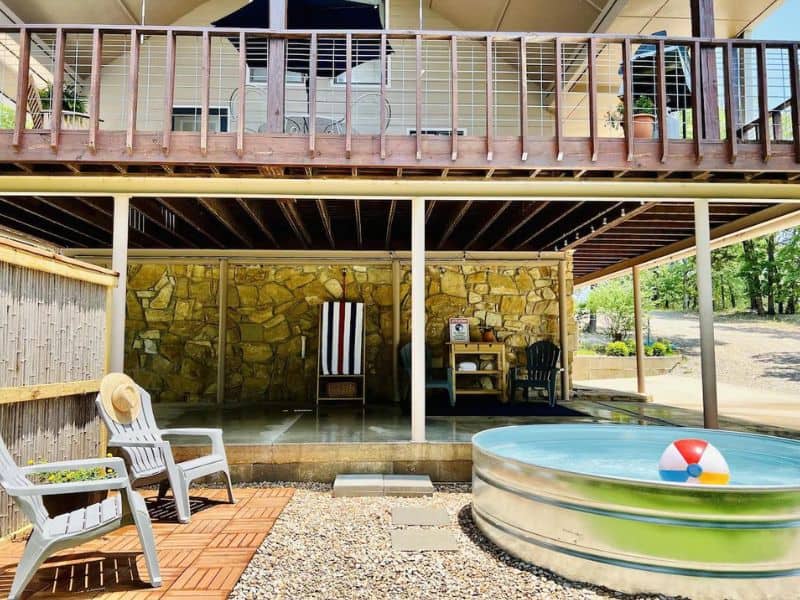 Outdoor area at "The Spot!" cabin rental near Turner Falls with a covered patio, lounge chairs, a cowboy pool with a beach ball, and a wooden upper deck.
