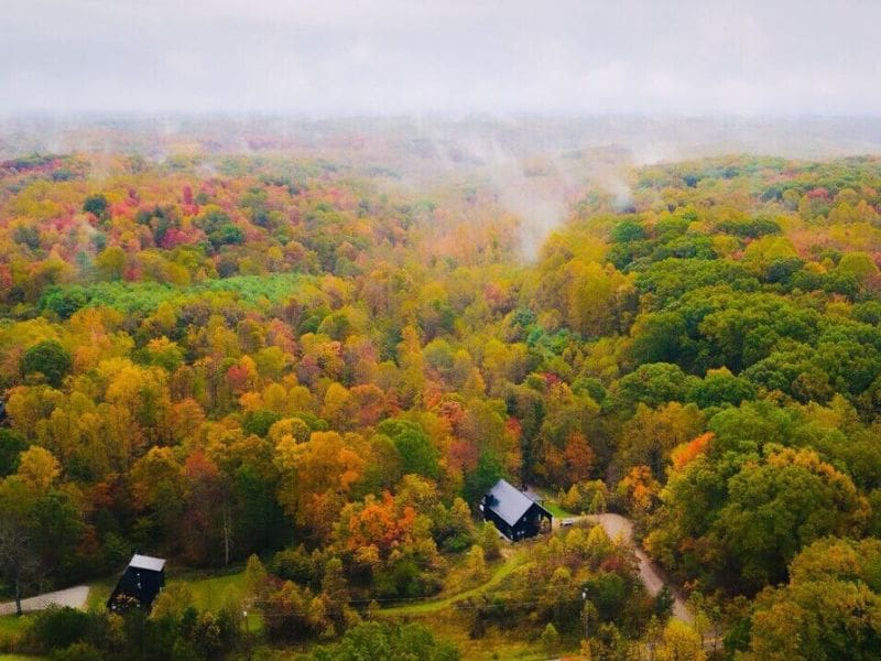 A breathtaking aerial view of Hocking Hills during fall, showcasing vibrant autumn foliage and two isolated cabins nestled among the trees. Cabin rentals in Hocking Hills, Ohio.