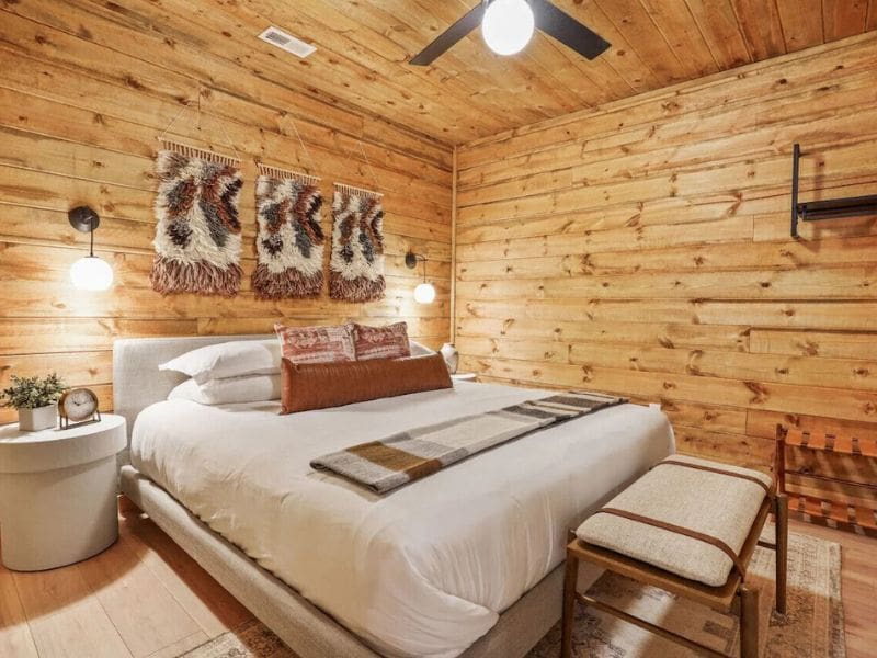 A cozy bedroom in The Everwood A-Frame, with Nordic-inspired decor and a king-size bed, textured wall hangings, modern lighting, and wooden walls. One of the Cabin rental in Hocking Hills, OH.