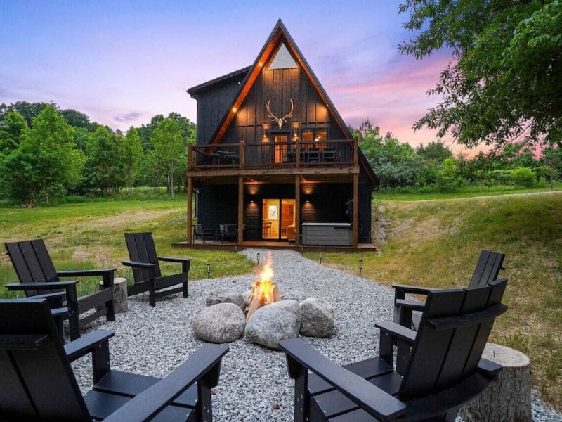 Exterior of The Everwood A-Frame in Hocking Hills, OH, featuring a black, modern A-frame cabin with a fire pit area surrounded by Adirondack chairs..