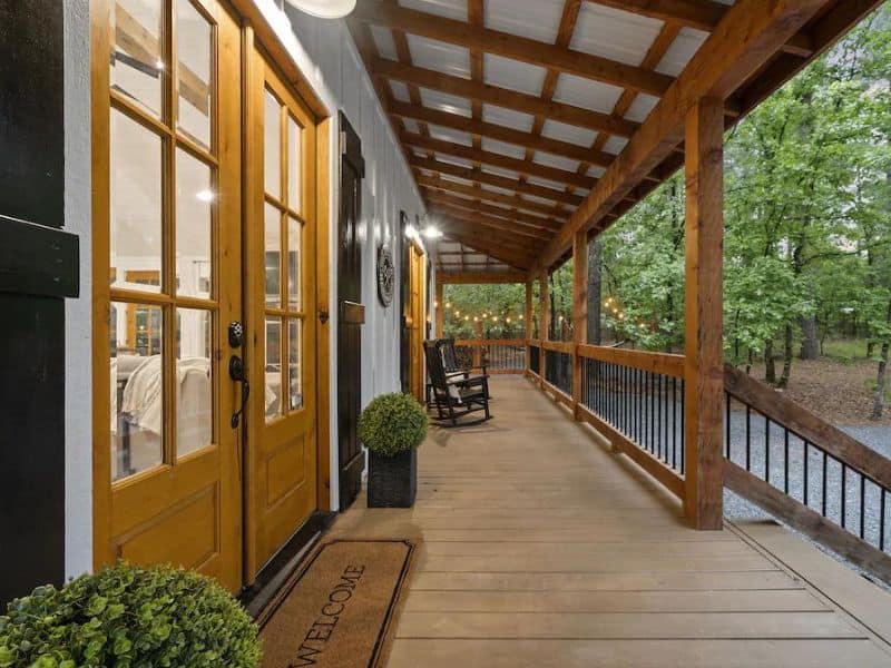 Front porch of a luxury cabin rental in Broken Bow with vibrant yellow doors, rocking chairs, and a 'Welcome' doormat.