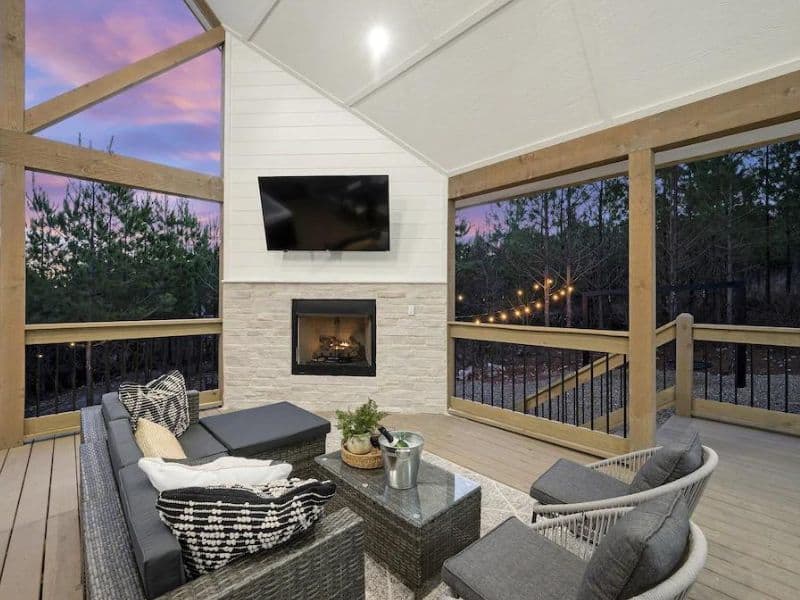 Covered outdoor seating area of Broken Bow cabin rental with a fireplace and mounted TV.