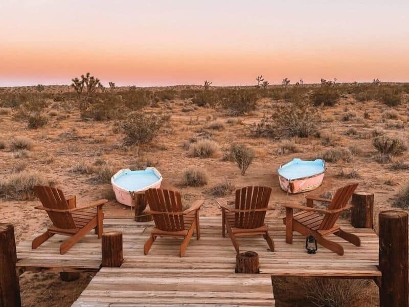 A deck with wooden Adirondack chairs overlooking the Joshua Tree desert and two beached rowboats at sunset. Design feature at Joshua Tree Vrbo - Flamingo Social Club