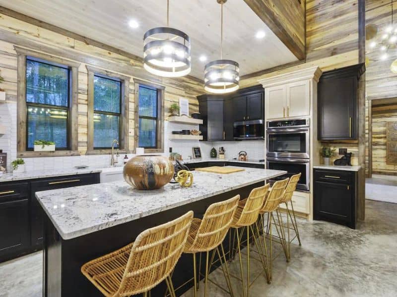 Interior of a 5-bedroom Broken Bow cabin rental featuring a modern kitchen with marble countertops, black cabinets, wicker bar stools, and dual pendant lights.