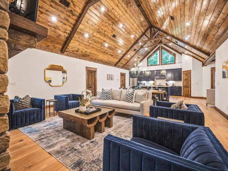 Inviting living room inside Boondock Bliss, a large Broken Bow cabin rental, with plush blue sofas, a large wooden coffee table, and exposed wooden beams.