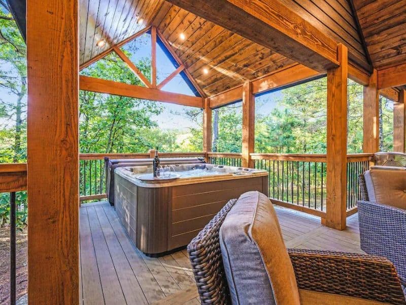 Covered outdoor hot tub on a wooden deck surrounded by trees at Boondock Bliss Vrbo rental in Broken Bow, OK.