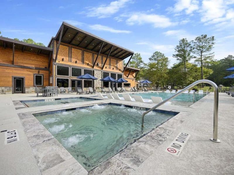 Community pool area with a hot tub and lounging chairs at a Broken Bow cabin complex, showcasing poolside amenities for guests.