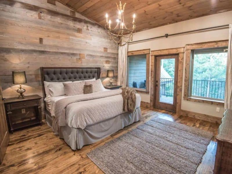Master bedroom in a Broken Bow large cabin rental, with a tufted headboard, rustic wooden walls, and doors leading to a balcony.