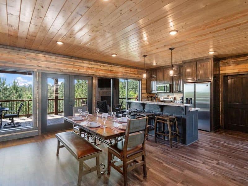 Dining and kitchen space inside a 5-bedroom Broken Bow cabin rental with a wooden dining table set, modern appliances, and sliding doors opening to a deck.