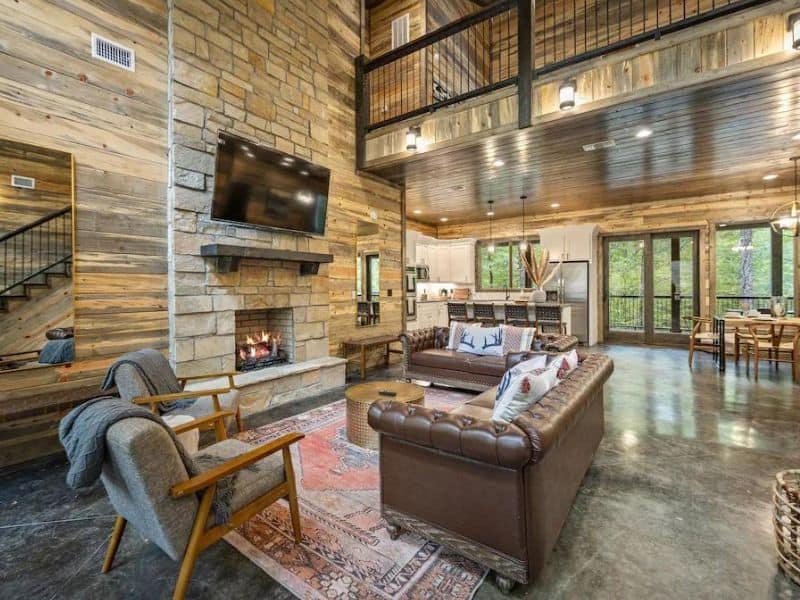 Spacious living room with high ceilings and a stone fireplace in a Broken Bow large cabin rental, complete with comfortable leather sofas and a mounted TV.