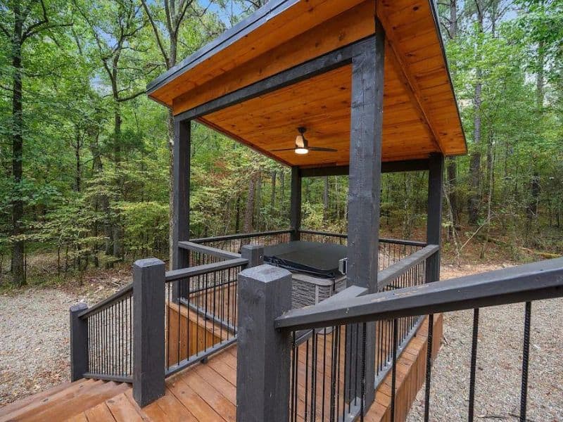 Covered outdoor hot tub on the deck of a Broken Bow Vrbo cabin rental, set against a forested backdrop.