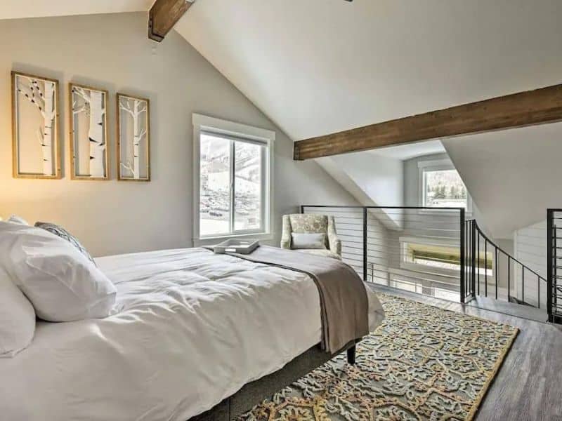 Loft bedroom with exposed beam and balcony overlooking the snowy landscape in Park City, Utah.