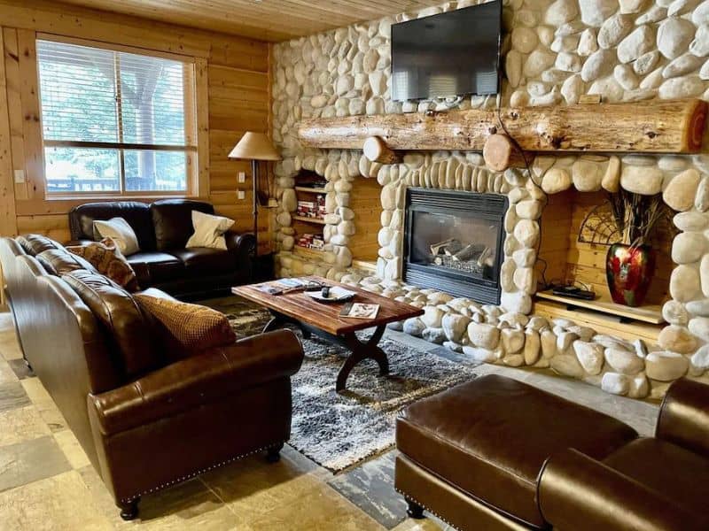 Cozy living room at Black Bear Lodge 209 in Park City with leather sofas, a rustic stone fireplace with a log mantel, and a wall-mounted TV.