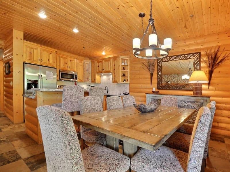 Dining area and kitchen of Black Bear Lodge 209 rental in Park City, with a large wooden dining table surrounded by patterned upholstered chairs and a modern kitchen in the background, complete with wood cabinetry and stainless steel appliances.