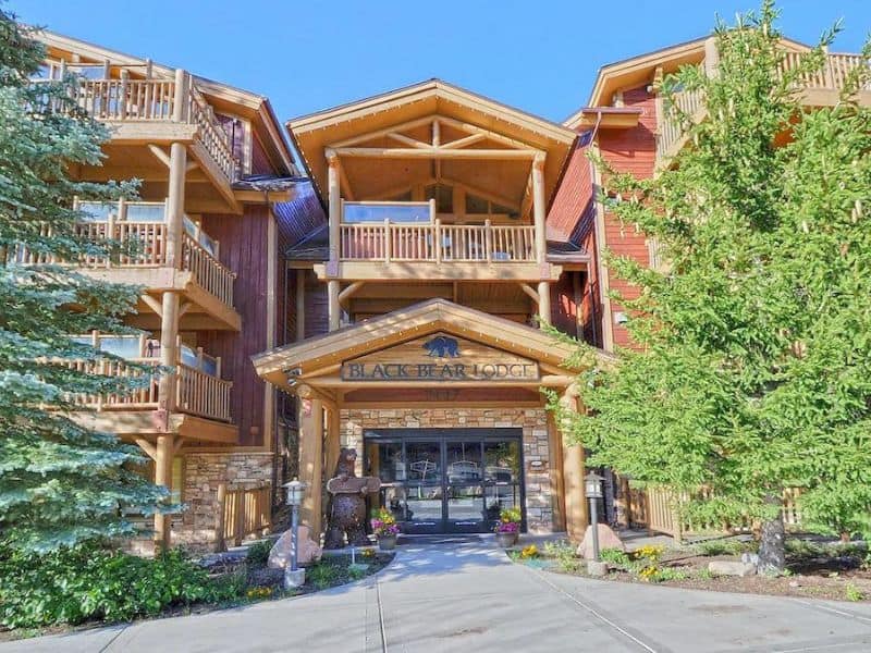 Exterior view of Black Bear Lodge, highlighting the lodge’s log cabin architecture, spacious balconies, and entrance surrounded by greenery. A highly rated ski-in, ski-out destination in Park City.