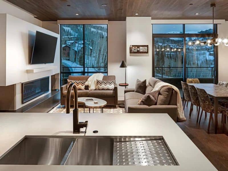 Spacious living room in a Luxe Empire Pass Condo in Park City featuring leather sofas, a modern fireplace, and large floor-to-ceiling windows with stunning mountain views.
