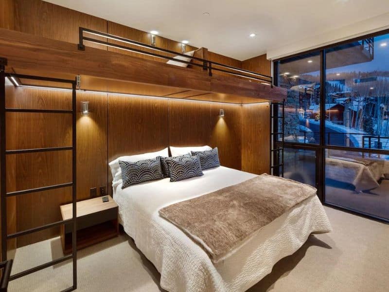 Elegant bedroom in a Luxe Empire Pass Condo rental in Park City with a plush king-size bed, modern alpine decor, and access to a private balcony overlooking snowy ski slopes.