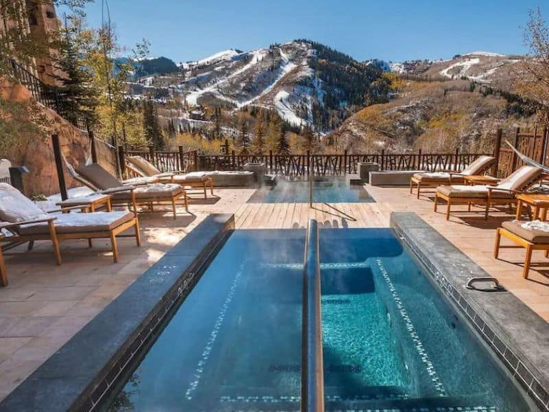 Stunning outdoor patio outside of a luxurious Empire Pass Condo rental in Park City with a steaming hot tub surrounded by snowy mountains and ski runs.