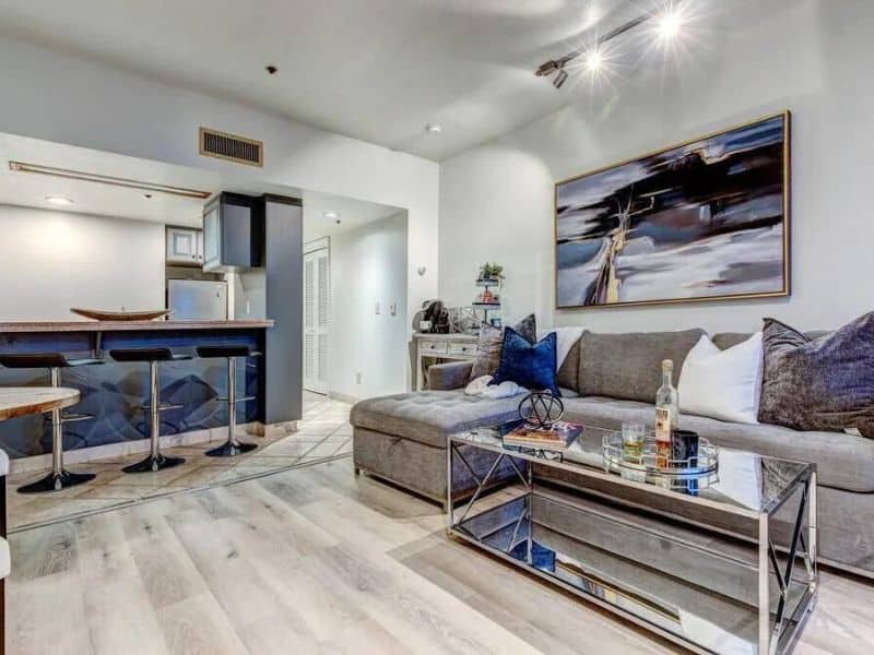 Spacious and well-lit living area of a ski in ski out Park City rental, featuring a large couch with blue pillows and a contemporary art piece, adjacent to the kitchenette and dining space.