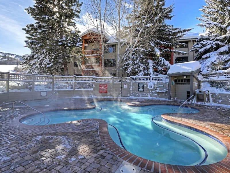 Outdoor heated pool surrounded by snow-covered trees at a Park City condo complex.