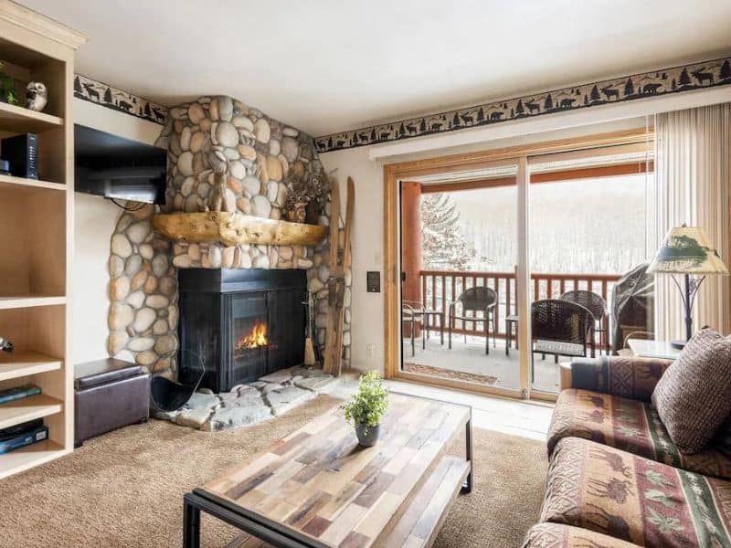 Cozy living room with a stone fireplace and forest view from the balcony in a Park City ski in ski out studio rental.