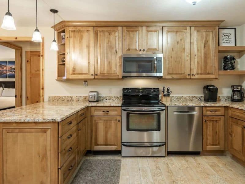 Modern kitchen with natural wood cabinets and stainless steel appliances in a ski in ski out Park City rental, featuring a granite countertop and pendant lighting.