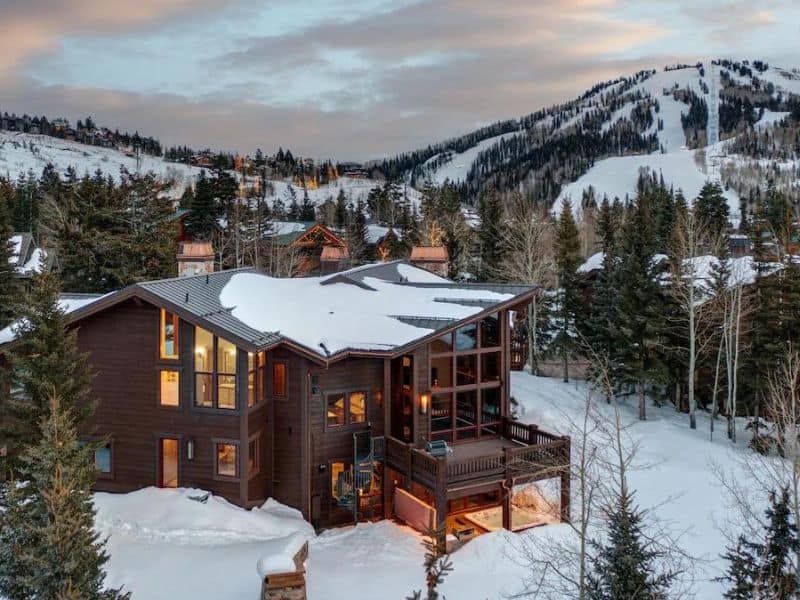 A large wooden ski in ski out rental cabin in Park City surrounded by snowy mountains.