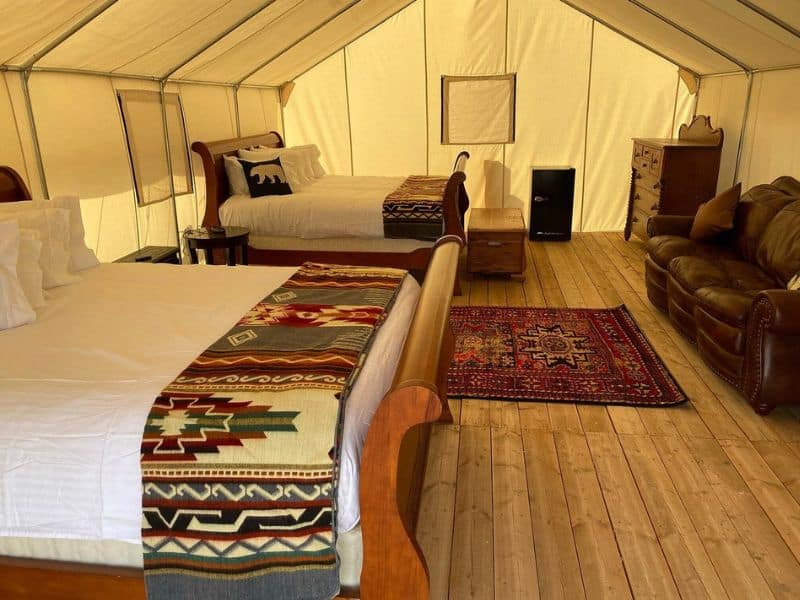 Interior of a glamping tent at Yellowstone Dreamin Camp, furnished with comfortable beds and a leather sofa, providing a cozy retreat.