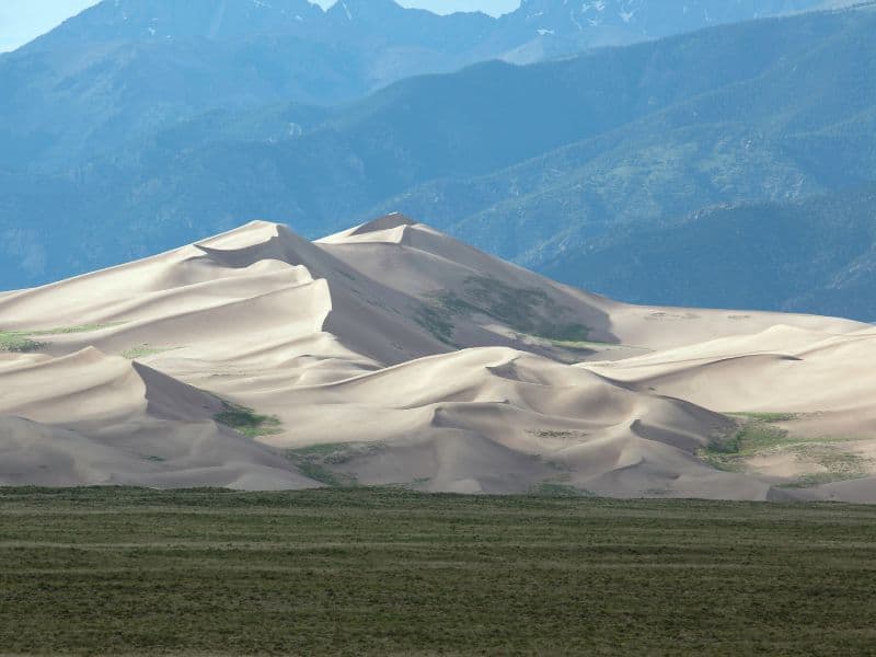 View of sand dunes in Great Sand Dunes National Park, Colorado with mountains in a background. A great add-on to a Denver to Grand Canyon road trip.