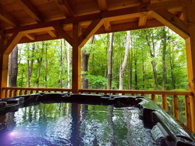 Covered outdoor deck with a large hot tub with a view of the surrounding forest.
