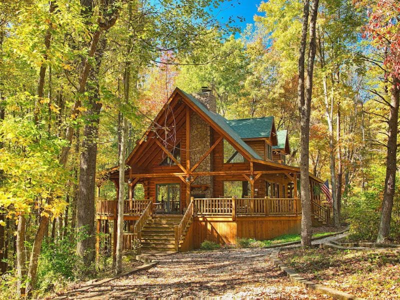 Redwood Lodge: Beautiful log cabin in the woods with an expansive wraparound porch. The cabin is surrounded by trees with autumn leaves. Hocking Hills cabin rental.