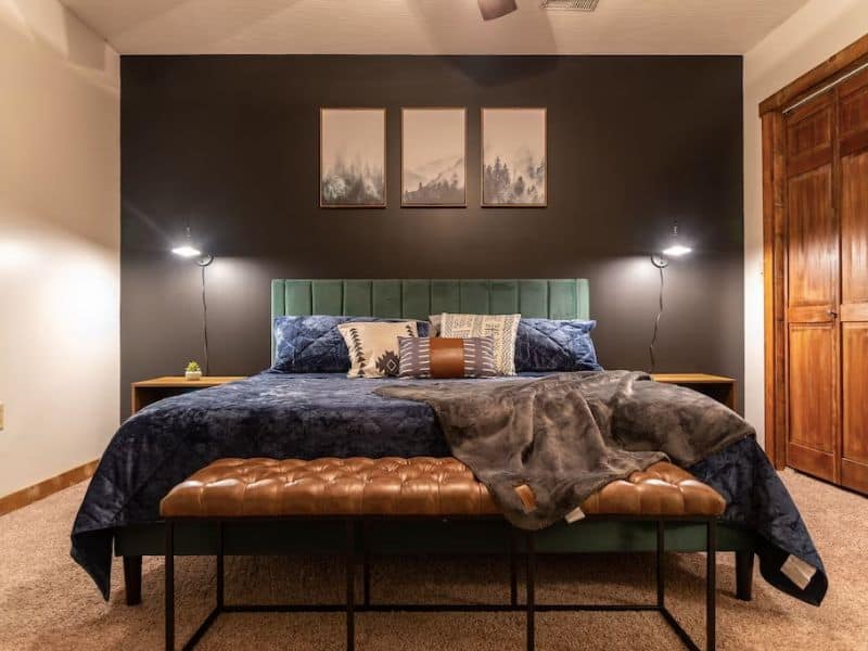 Mid-century modern bedroom with emerald green headboard, leather footrest and black accent wall