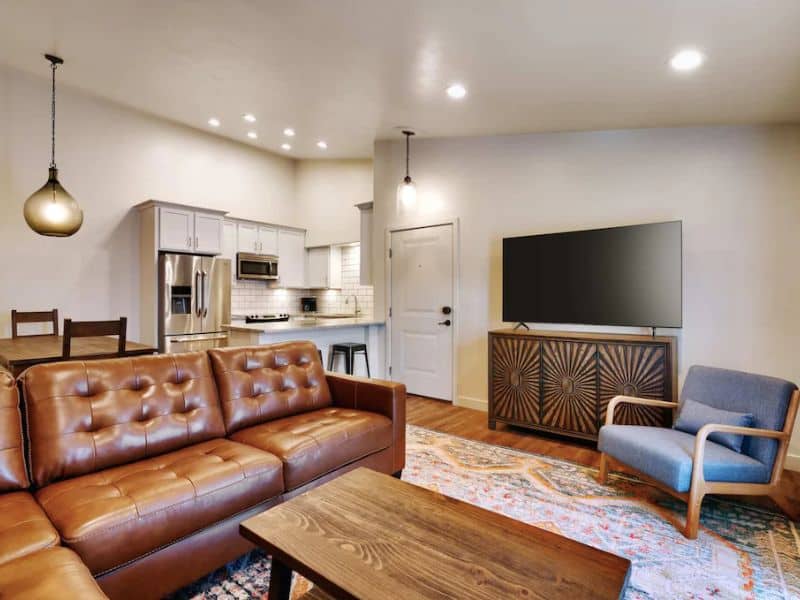 Modern living area with brown leather couch, large tv, and well equipped kitchen at Moab airbnb property