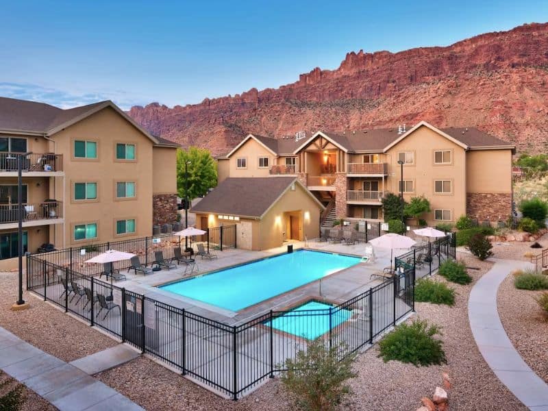 Exterior view of apartments with communal pool and hot tub in Moab Utah with red rocks in the background