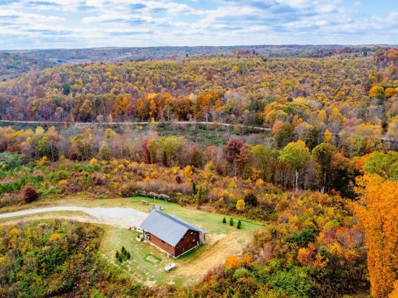 Aerial View of Shurtz Overlook pet-friendly cabin rental in Hocking Hills, OH: A bird’s-eye view of the cabin surrounded colorful Fall foliage. There's a clear view of the cabin’s proximity to hiking trails and open landscapes.