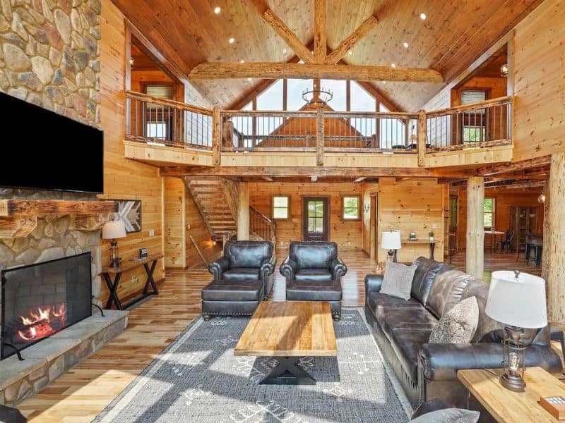 Interior view of a spacious living room with a stone fireplace, leather couches, and a loft in a large cabin in Hocking Hills, ideal for group stays.