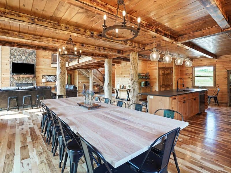 Large dining area with a long wooden table, modern kitchen, and industrial-style lighting in a Hocking Hills cabin, perfect for family gatherings.
