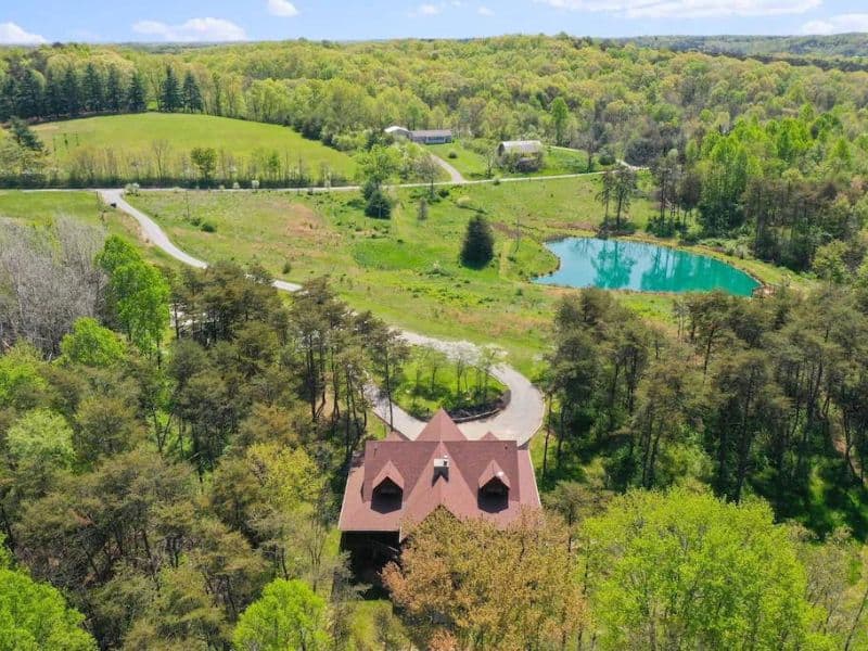 Aerial view of large Hocking Hills cabin surrounded by woods, greenery, and a pond