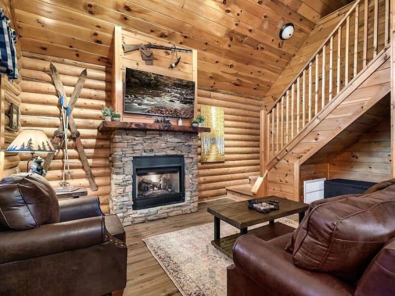 Living area of Pigeon Forge vacation cabin with log siding, stone fireplace, leather couches and rustic decor.