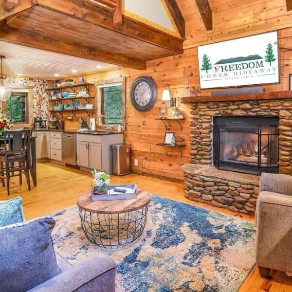 Living area of Pigeon Forge vacation cabin with stone fire place, wood paneling, rustic detailing and dining area beyond.