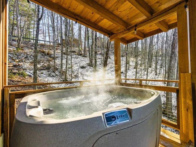 Outdoor jacuzzi tub of Pigeon Forge vacation cottage, on wooden covered porch, and views of surrounding forest.