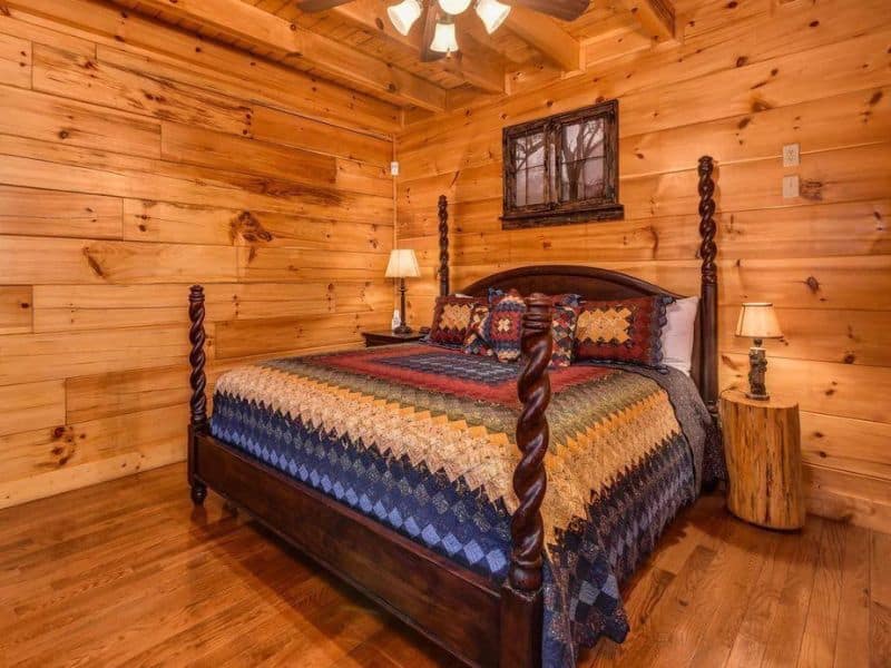 Bedroom of Pigeon Forge rental cabin, with wood paneling, decorative quilted bedding, and rustic decor.