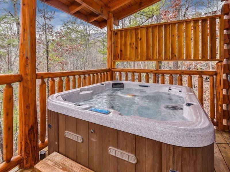 Outdoor jacuzzi tub on wooden porch overlooking forest views of Pigeon Forge vacation cabin.