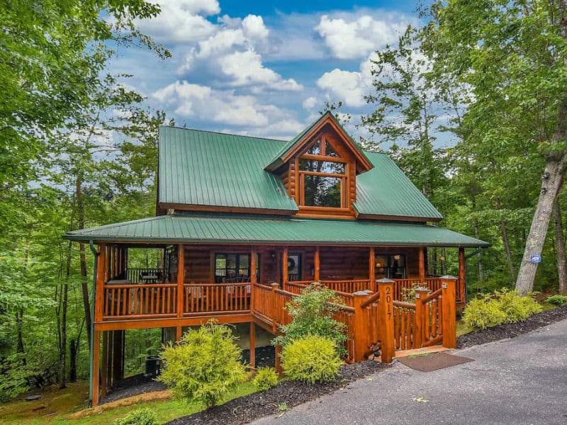 Exterior of Pigeon Forge rental cabin, with log cabin construction, wrap around porch, and surrounding forest.