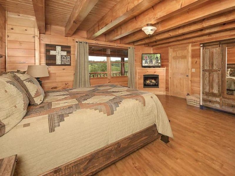 Master Bedroom of Pigeon Forge vacation cabin with wood beam ceiling, rustic accents, fireplace, and forest view.