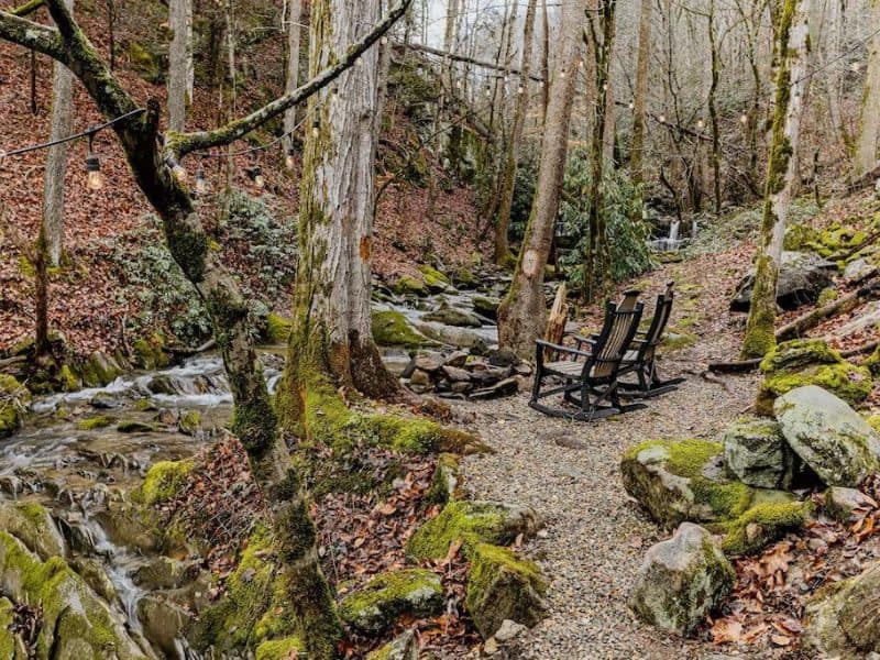 Outdoor shot of Pigeon Forge vacation home, river side seating area with decorative lighting and waterfall view.